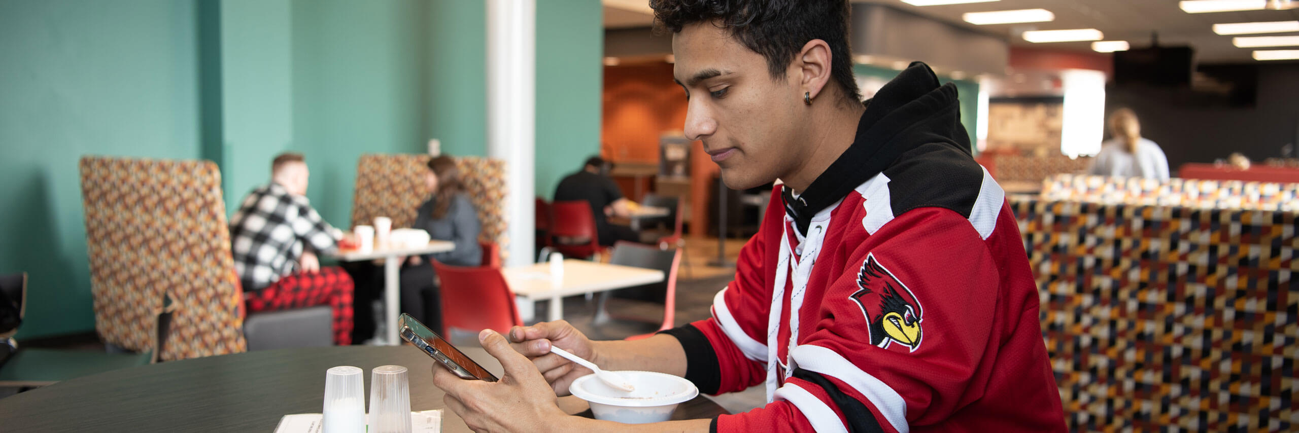 Student eats breakfast while looking at his phone.